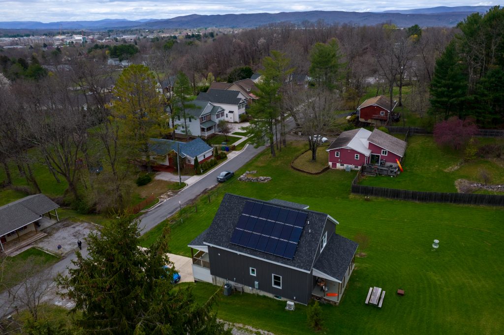 Image of house with solar panels in a neighborhood with mountains behind it.